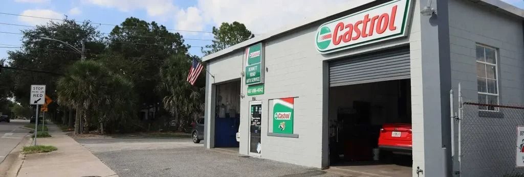 A gray Castrol auto repair shop with an open garage, a red car inside, and a street in front.