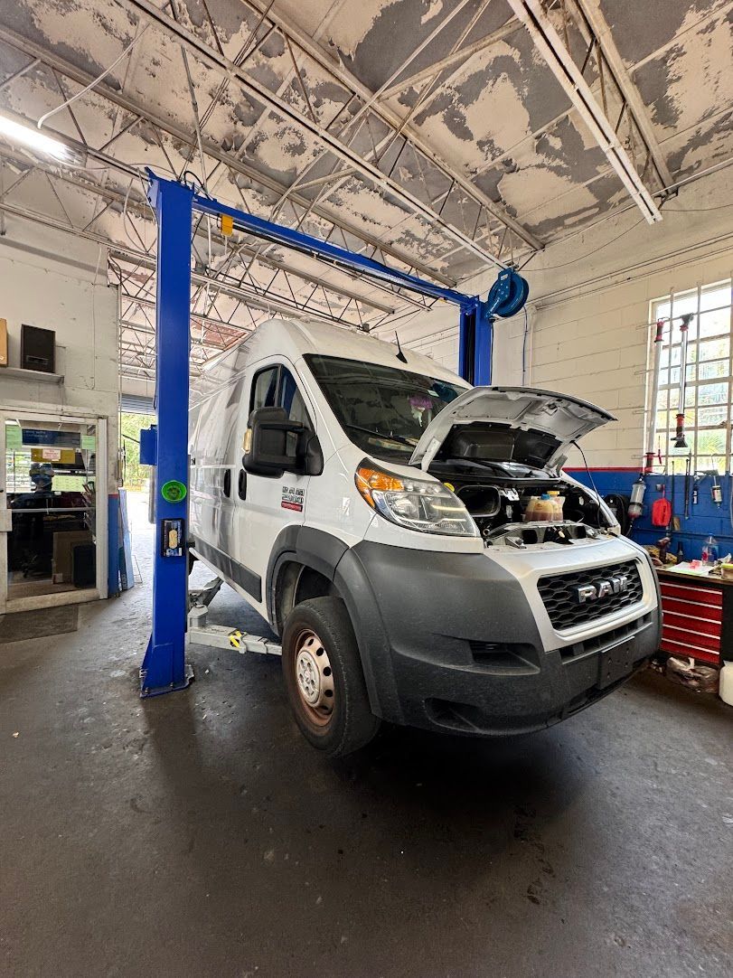 White RAM van on a lift in a garage with its hood open for service.