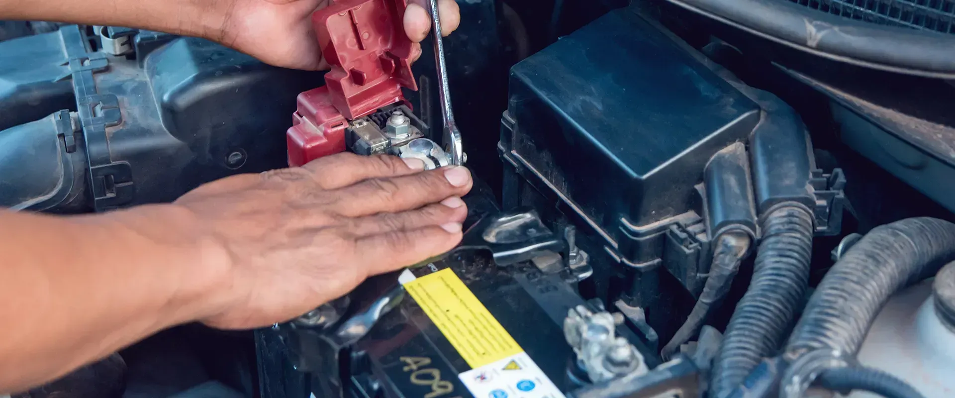 A person using a wrench to work on a car battery in an engine compartment.