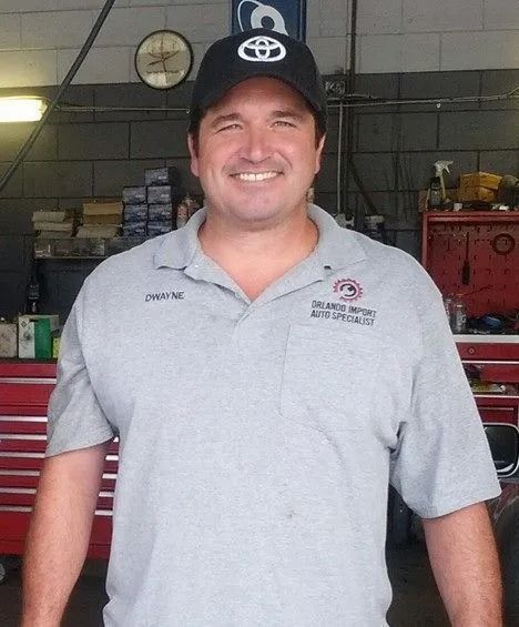 Mechanic in a Toyota hat smiles at the camera in a garage.