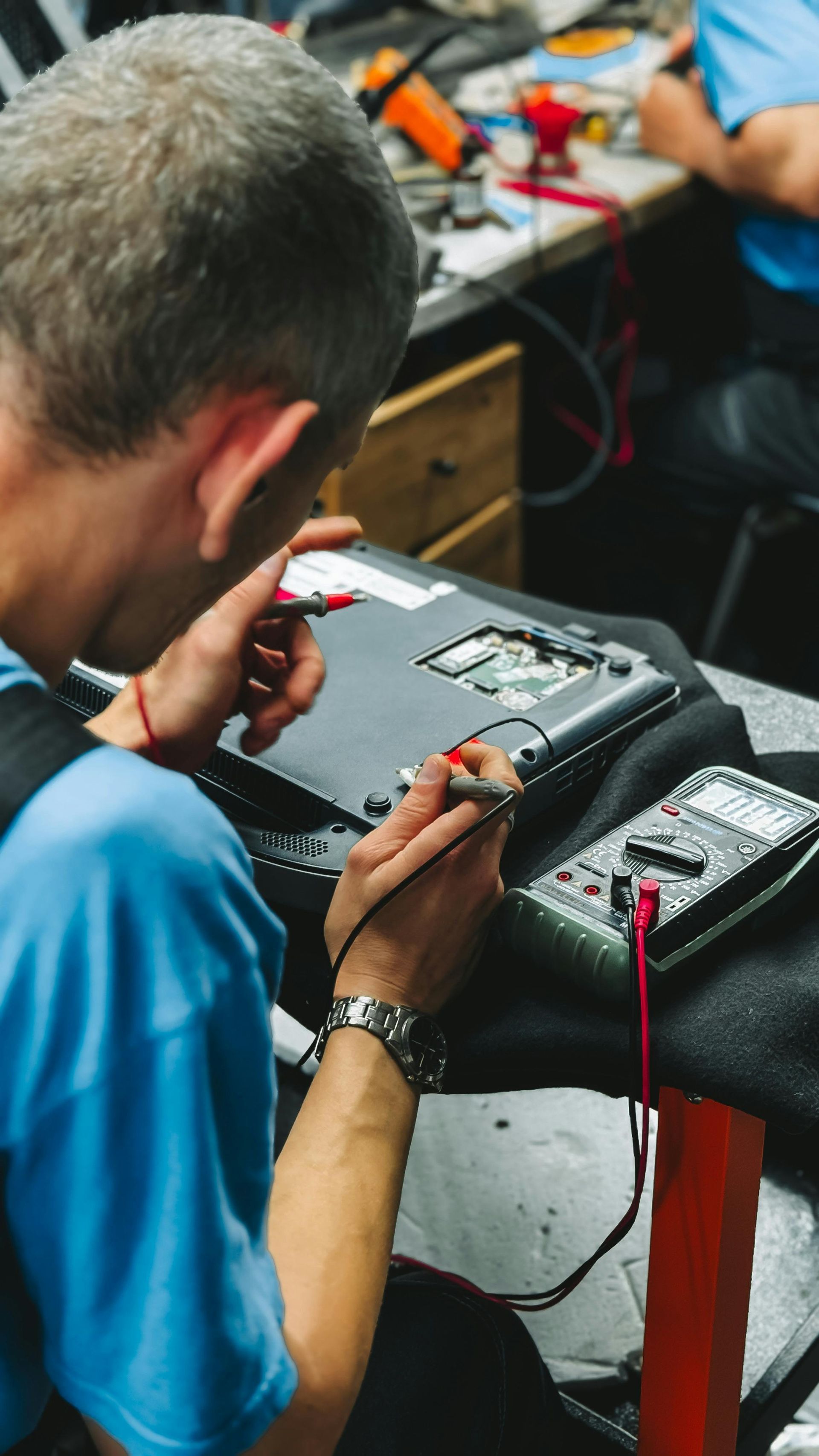 Person in blue shirt using multimeter to test laptop components.