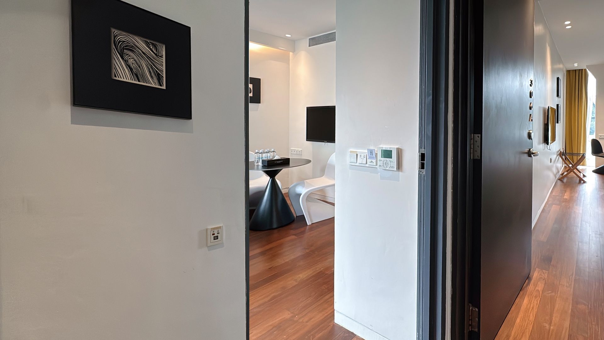 Hallway with wooden floor, ajar black door, and a glimpse into a white room with furniture.