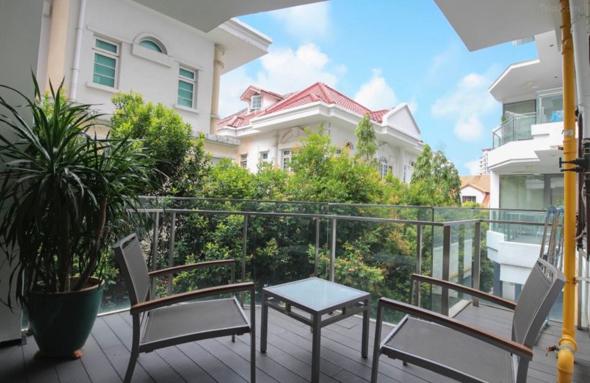 Balcony with two chairs and a small table, overlooking trees and buildings on a sunny day.