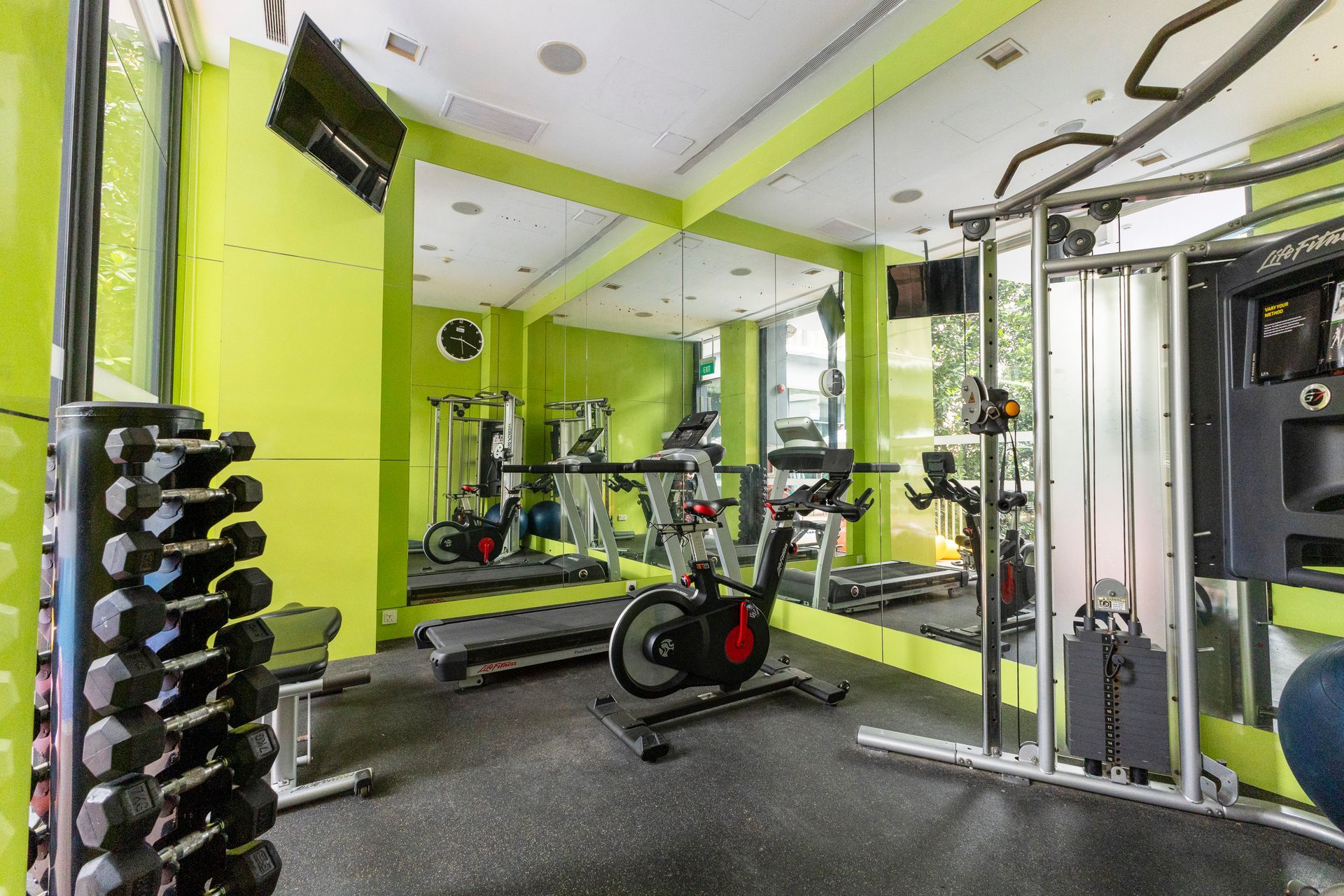Gym with weights, cardio machines, green walls, and mirrors.
