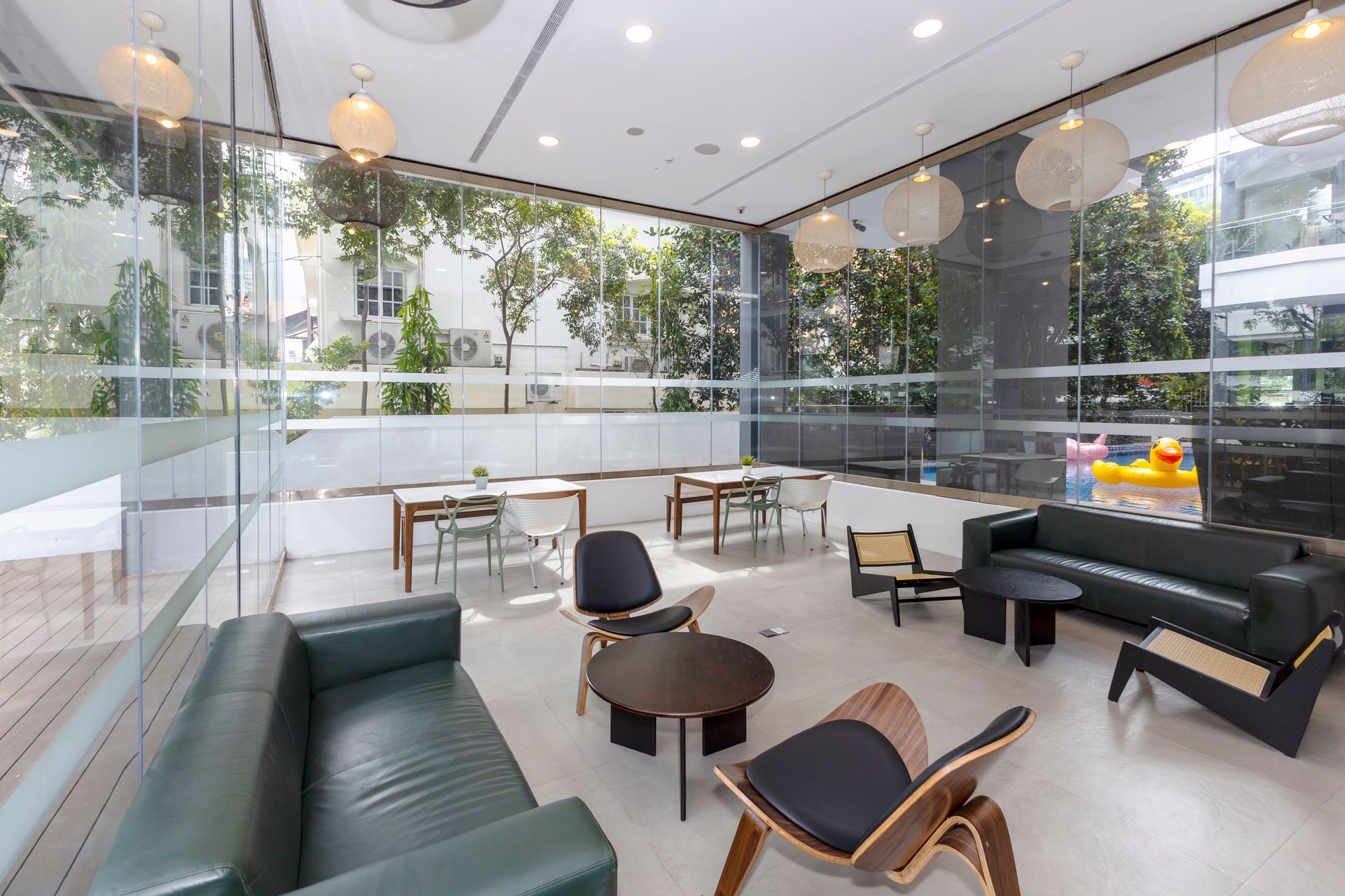 Modern lounge area with green couches, round tables, and glass walls overlooking greenery.
