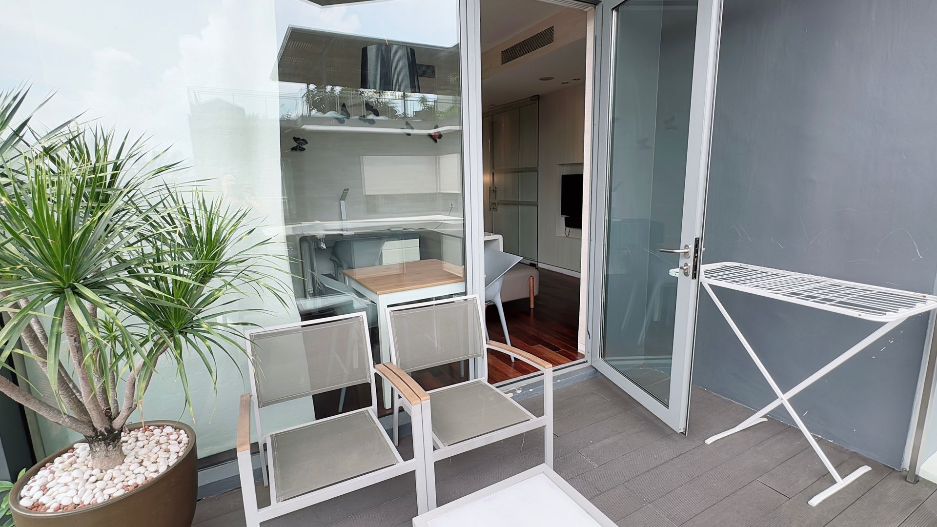 Balcony with two chairs, plant, and open glass doors leading to a room.