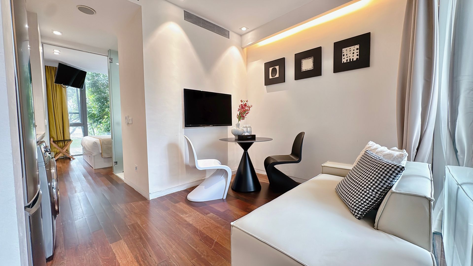 Small modern apartment with living area, dining table, and television on a white wall, hardwood floors.