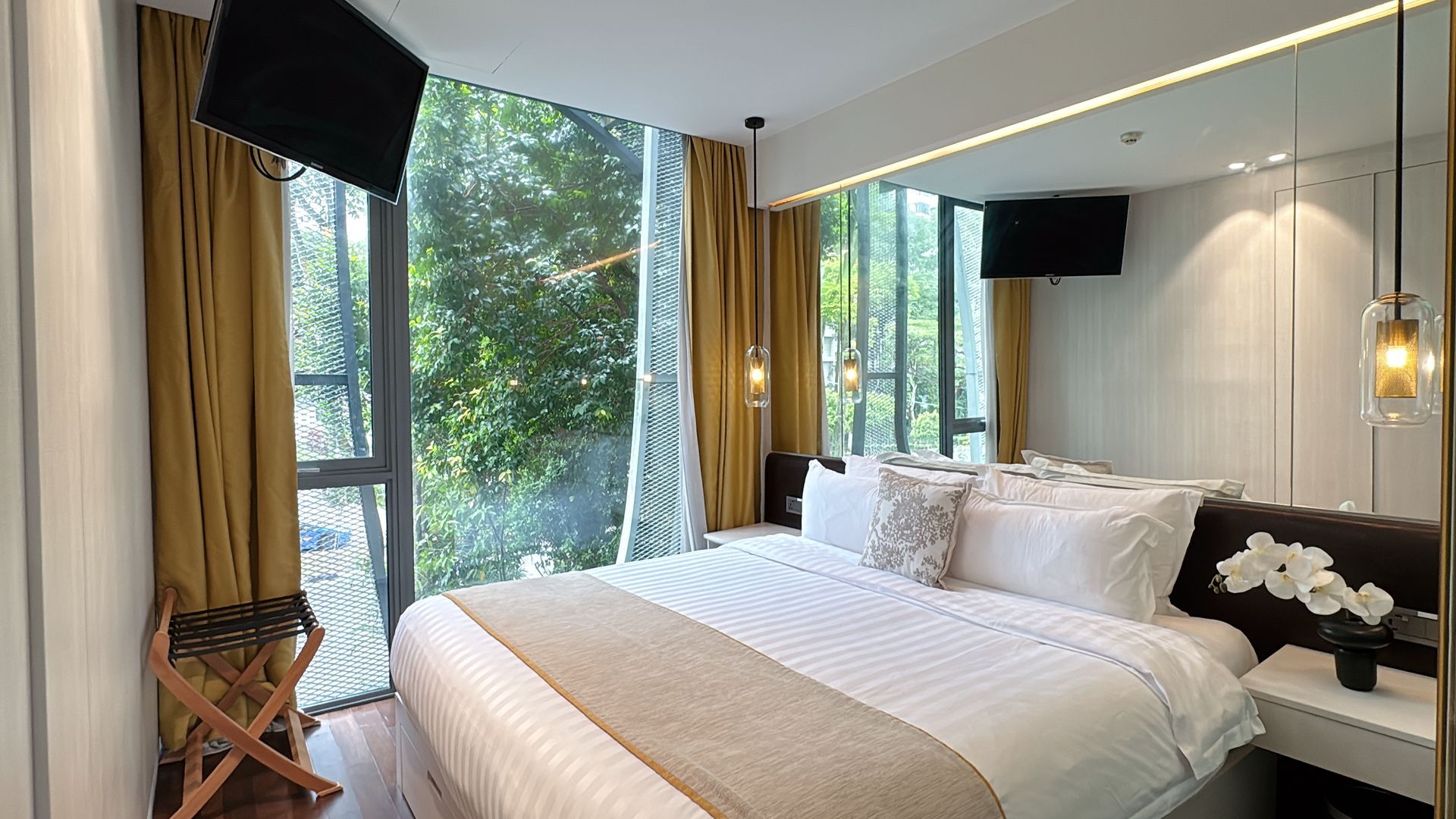 Bedroom with large windows, gold curtains, bed with white linens, mirrored wall, and small tv.