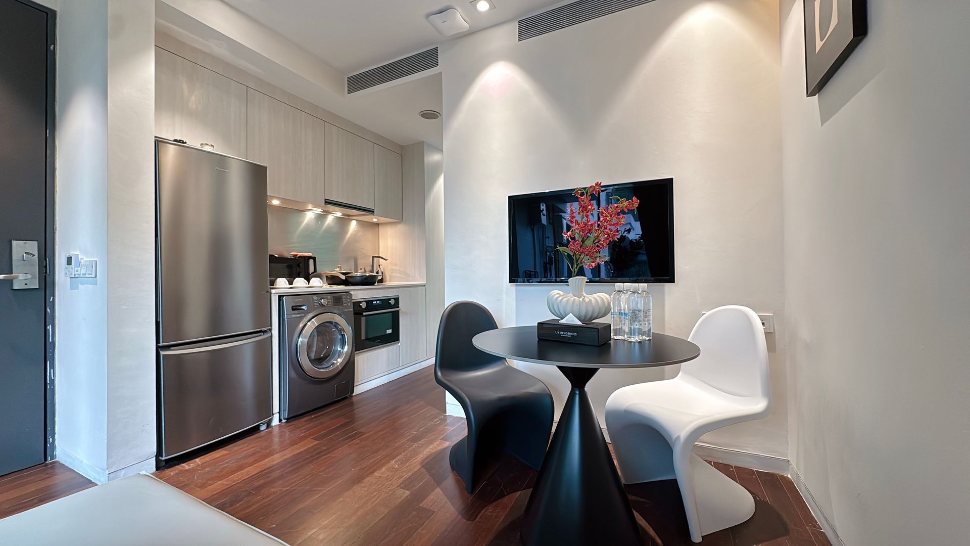 Small modern apartment: kitchen with stainless steel appliances, dining area with round table and two chairs.