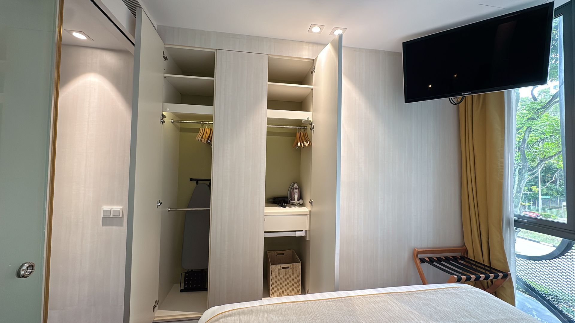 Bedroom closet with open doors, clothes hanging, and a TV mounted above the bed.
