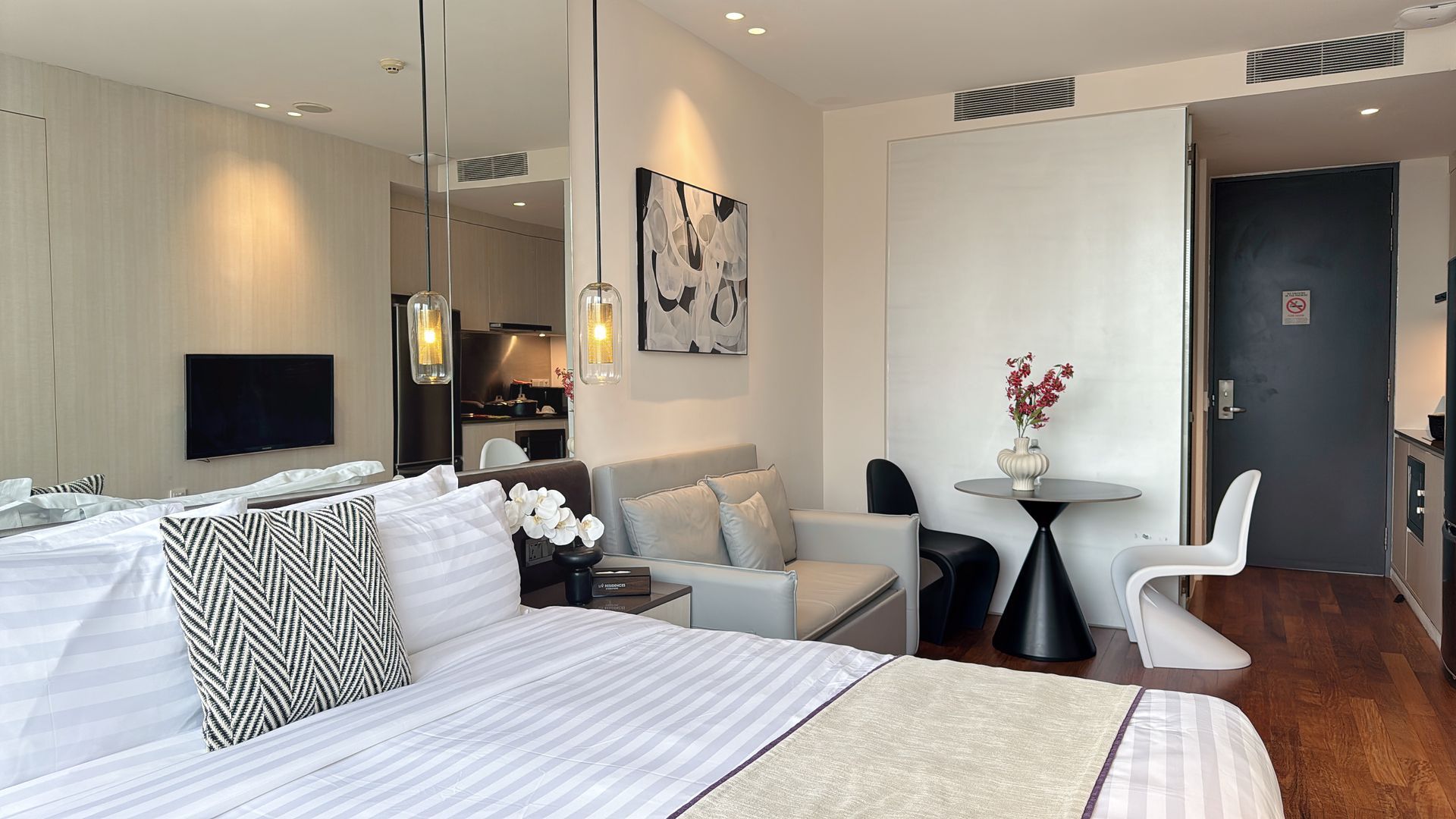Hotel studio with bed, small seating area, and kitchenette. White, neutral colors.