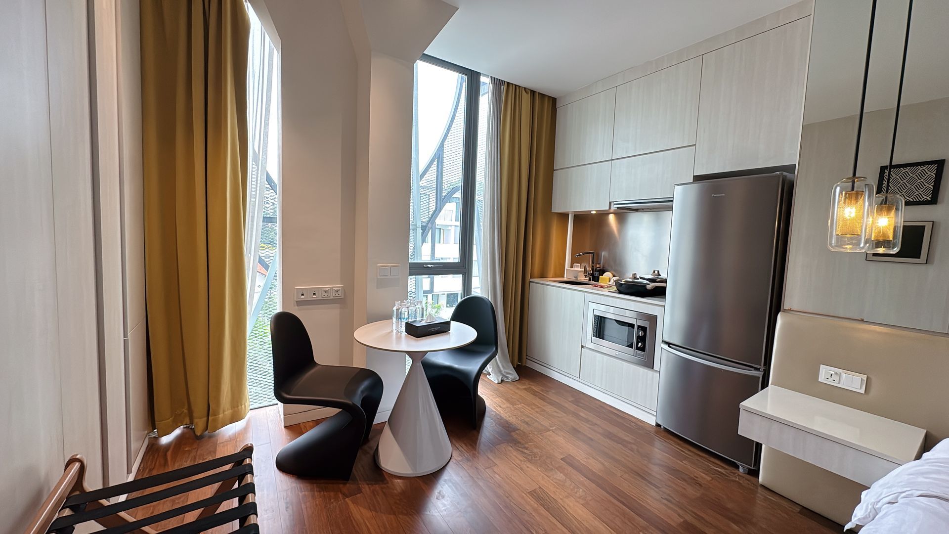 A modern studio apartment with wooden floors, small table and chairs near a window with mustard curtains.