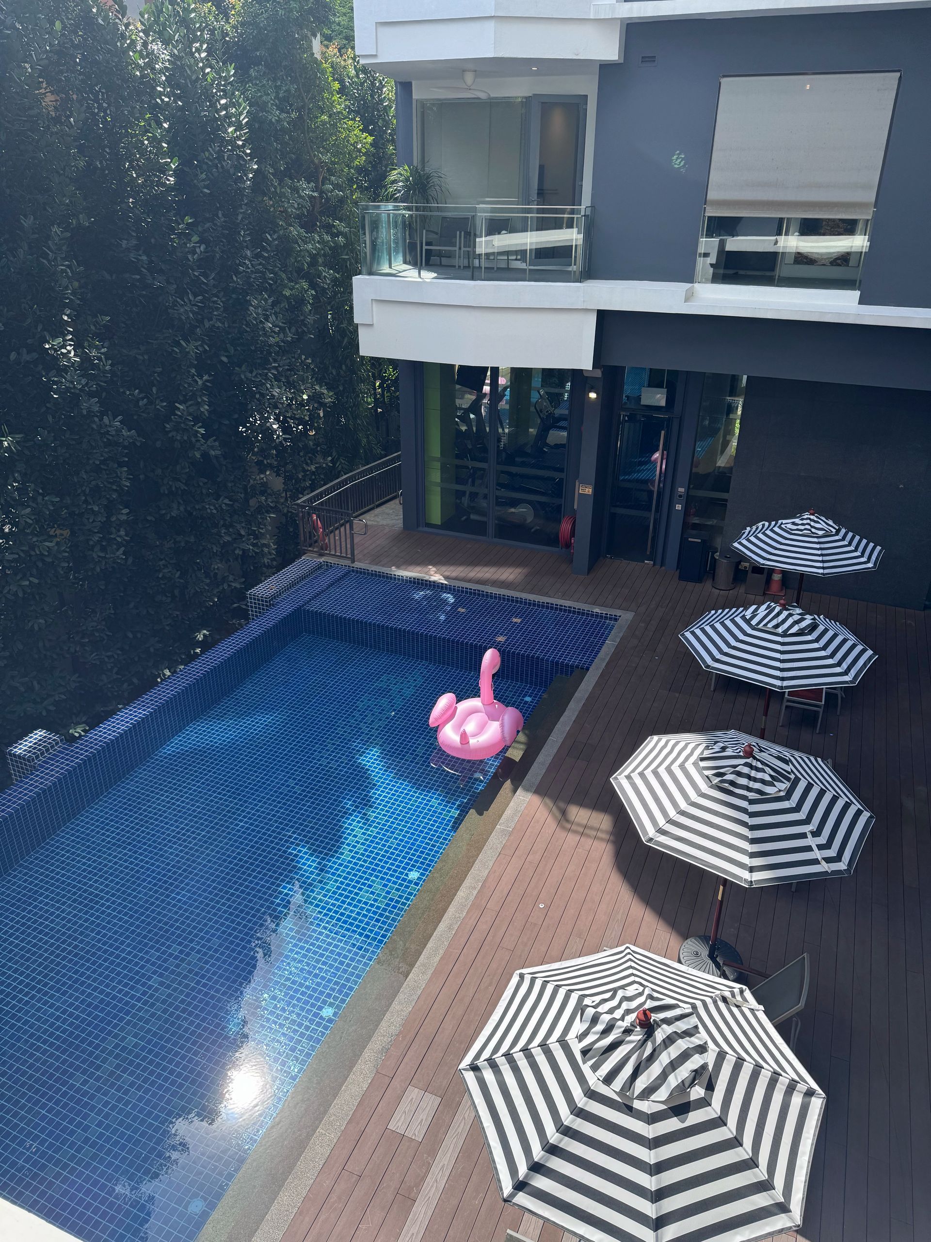 Poolside scene with a pink flamingo float, striped umbrellas, and a modern building.