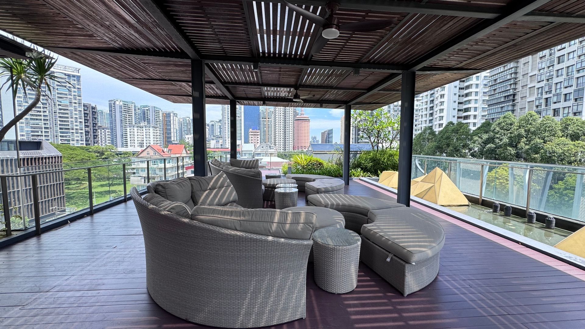 Outdoor lounge area with wicker furniture under a slatted roof; city skyline in the background.