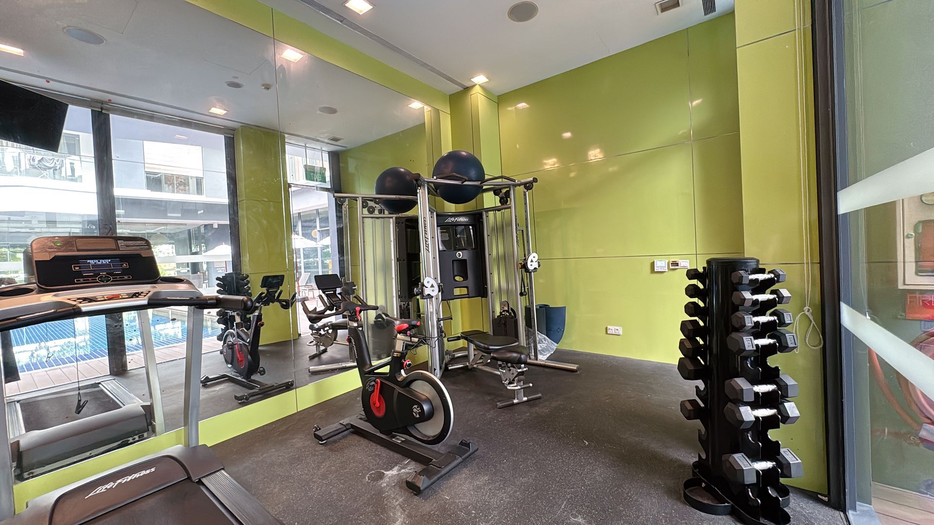Gym with exercise equipment: treadmill, bike, weights, and mirrored wall.