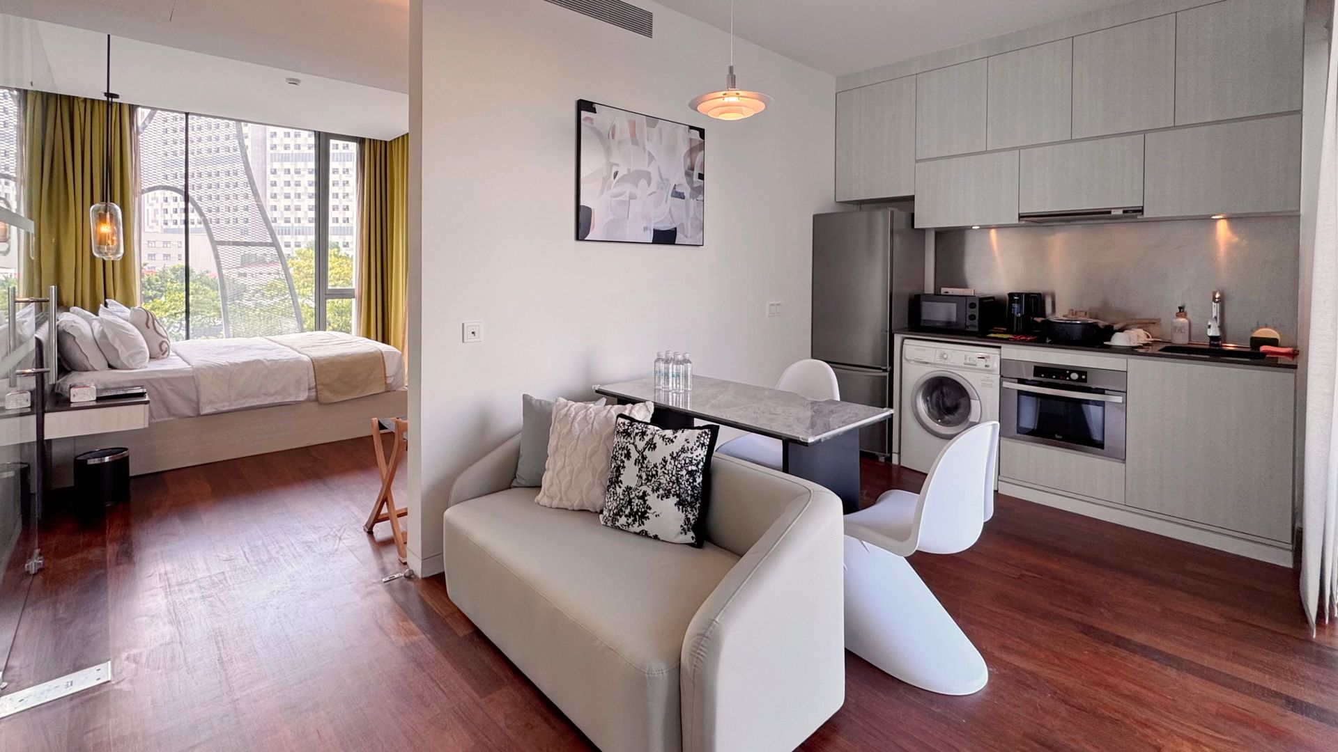 Studio apartment with open floor plan: bed, sofa, kitchen, and dining area with large window.