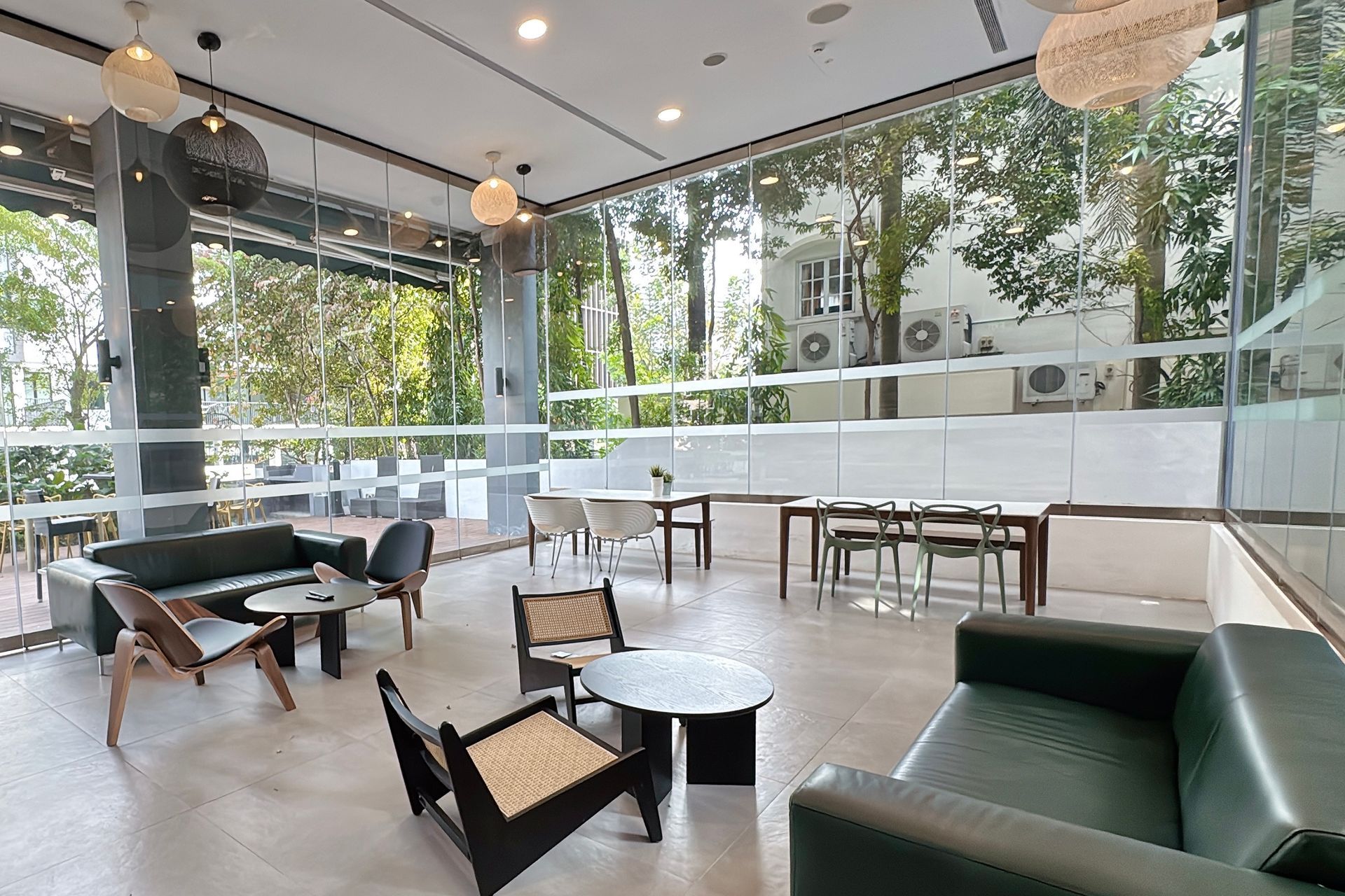 Modern cafe with floor-to-ceiling windows. Features seating areas with couches, tables, and chairs; light fixtures hang from the ceiling.