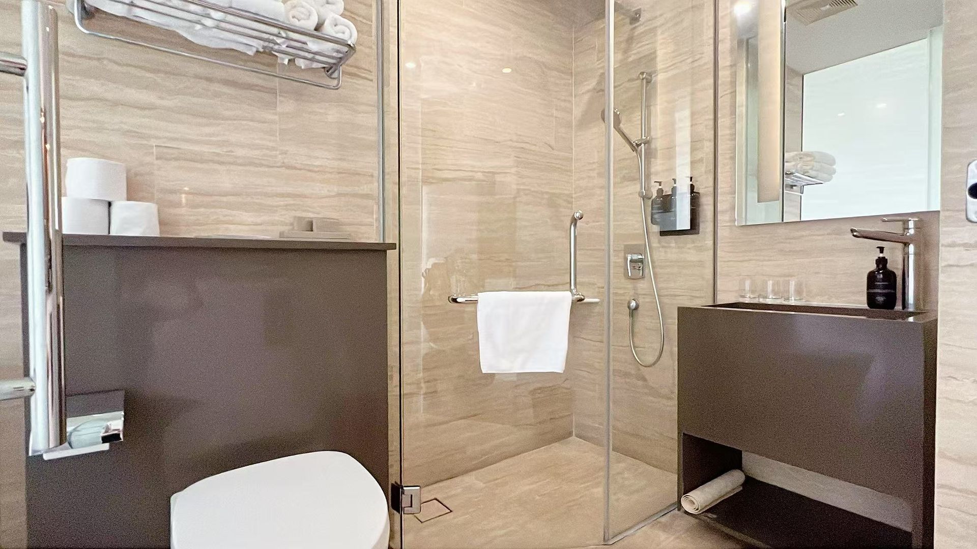 Modern bathroom with glass shower, toilet, sink, and neutral-toned tiling.