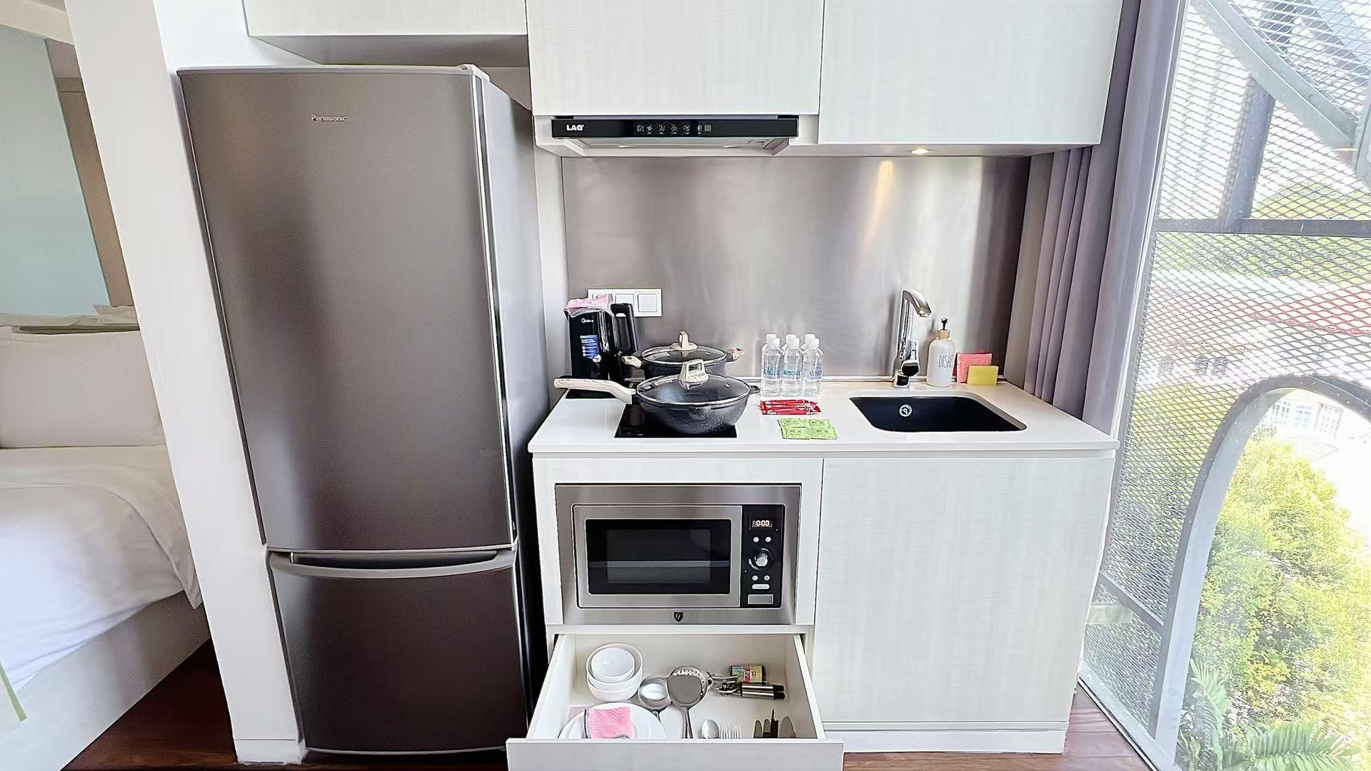 Small kitchen with refrigerator, microwave, sink, and cooktop. White cabinets and stainless steel appliances.