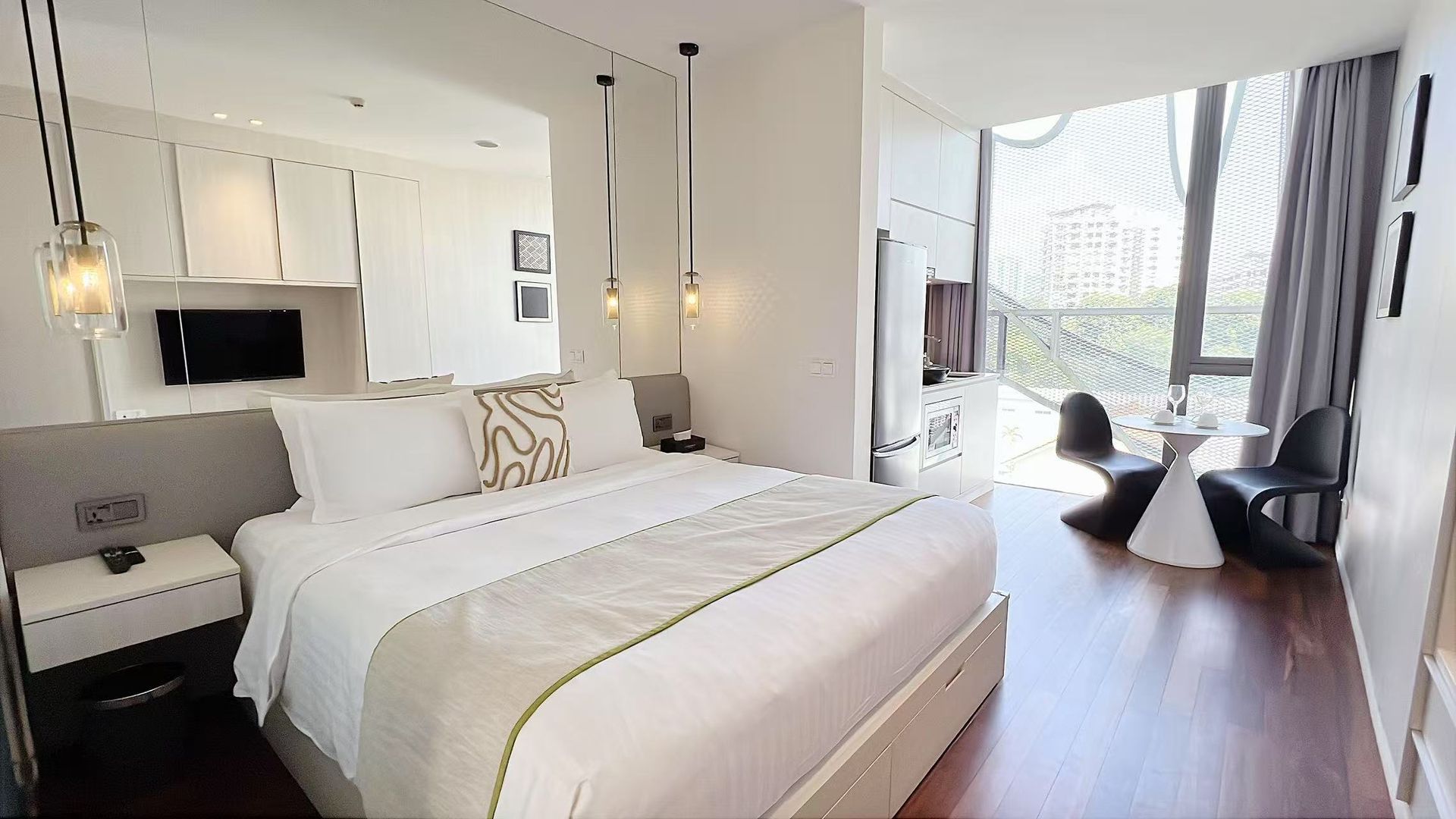 Bright hotel room with a king-sized bed, small table and chairs, and a large window.