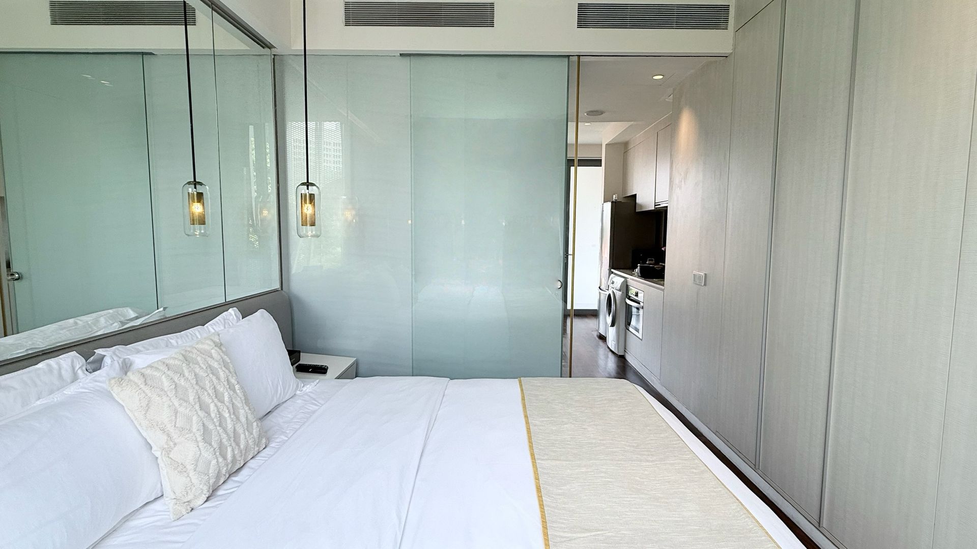 Bedroom with a bed, large mirror, glass divider, and a view to a small kitchenette.
