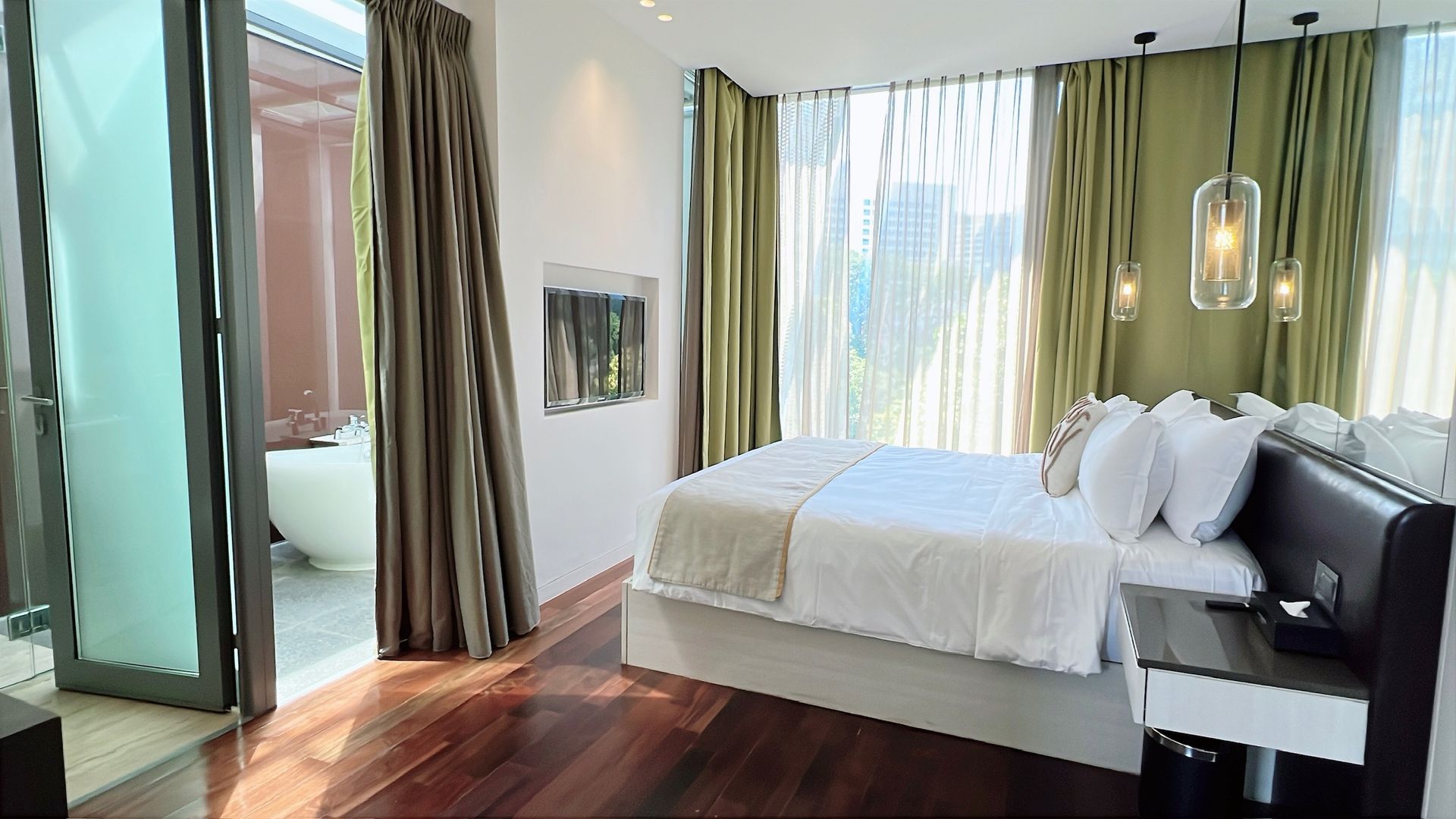 Bedroom with bed, nightstand, and curtains; view of a bathroom with a bathtub.