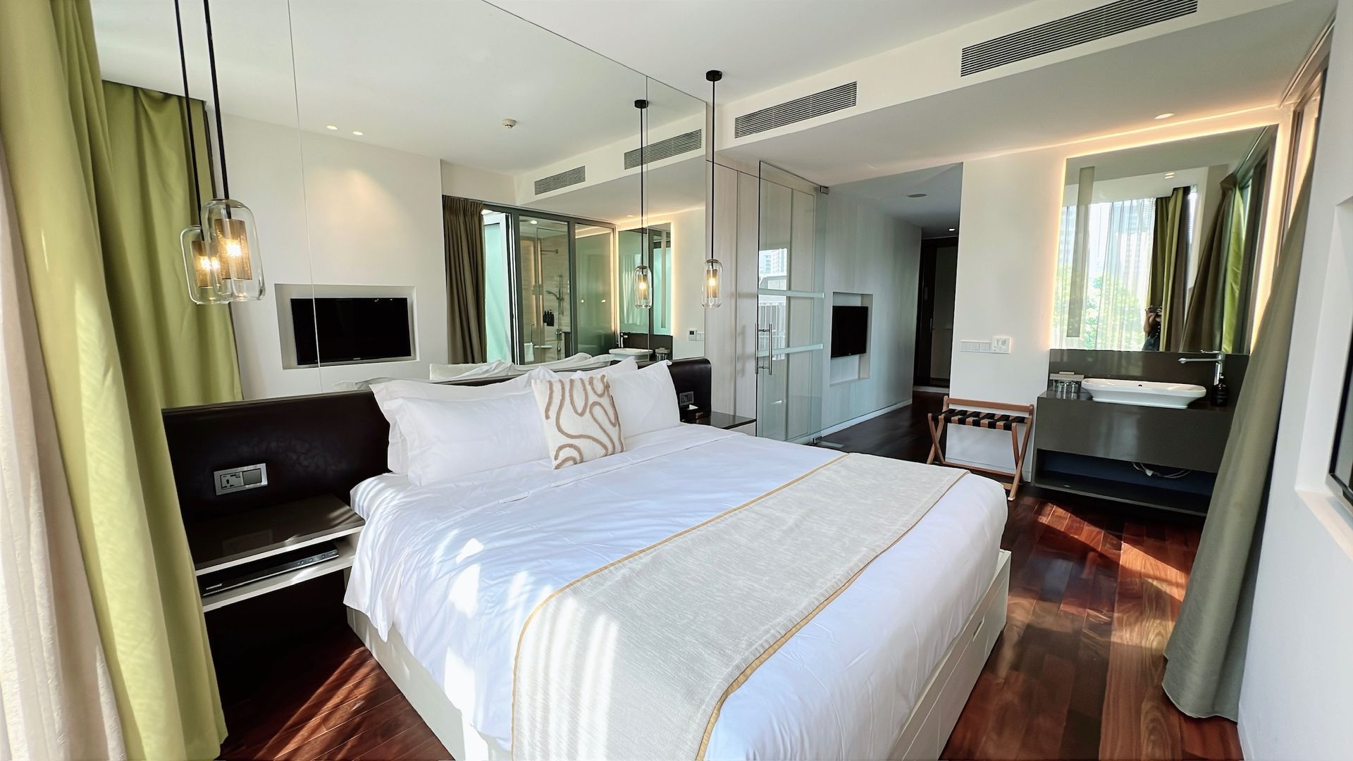 Hotel bedroom with a bed, dark wood floors, and large windows.