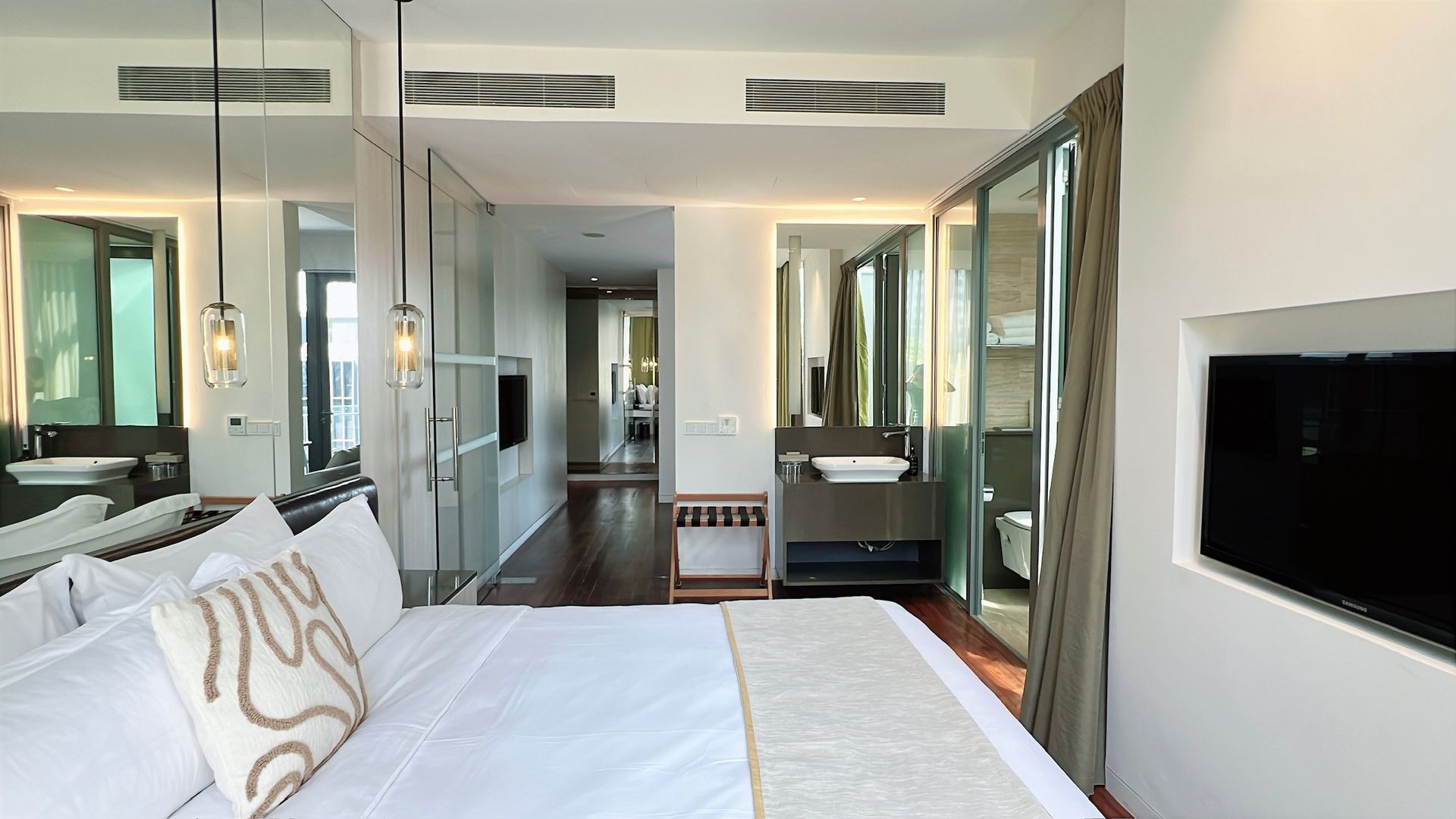 Modern hotel room with bed, bathroom, large mirrors, and a mounted TV.