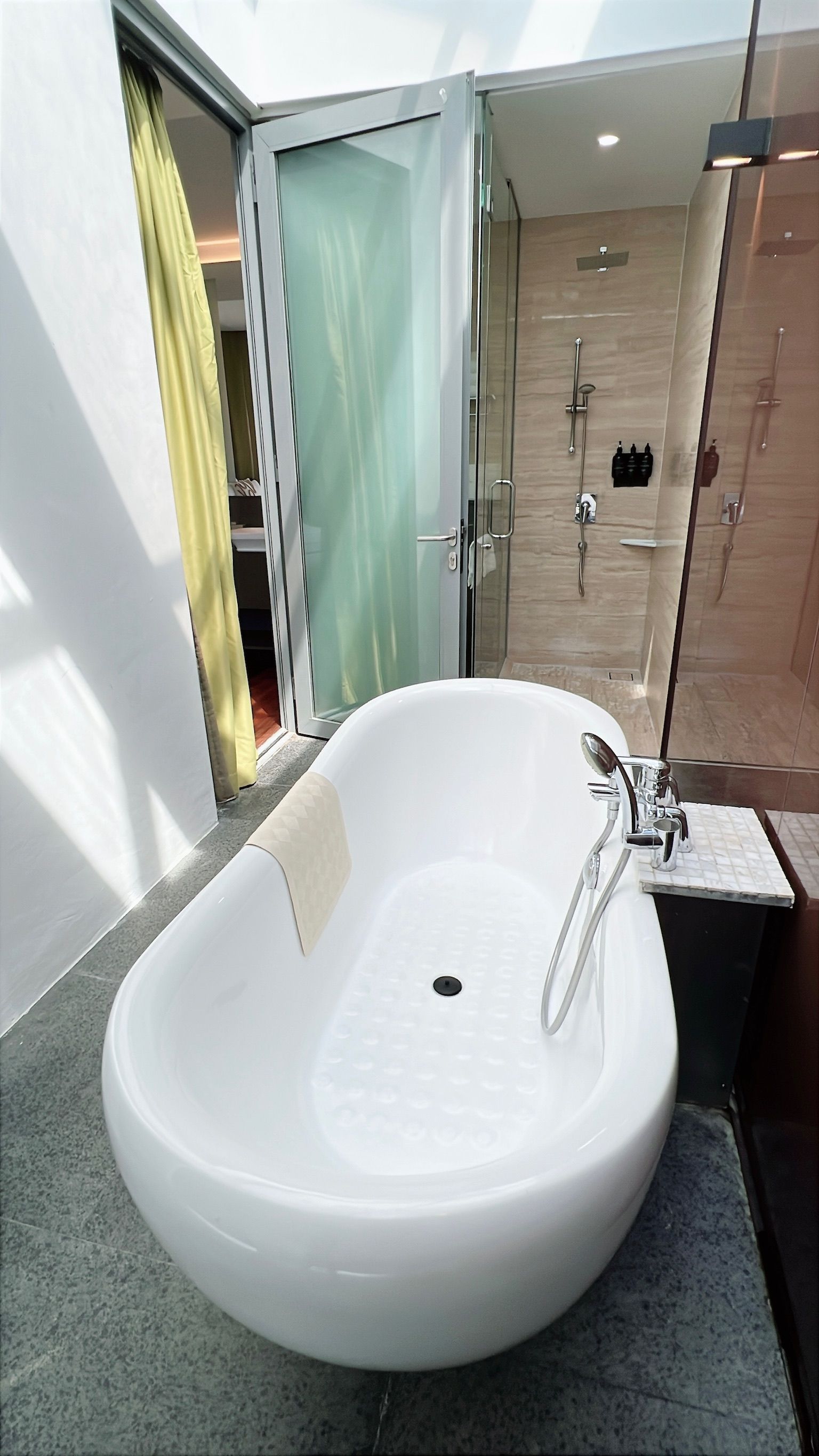 White oval bathtub in modern bathroom; glass shower in background.
