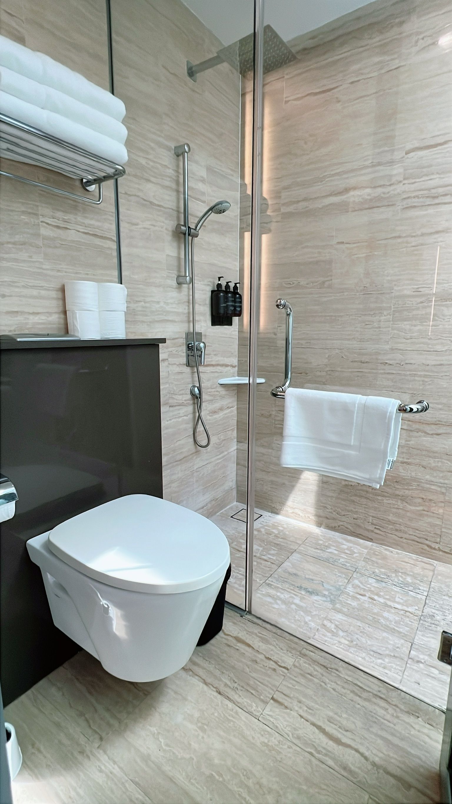 Modern bathroom: toilet, shower with glass door, towels, and toiletries.