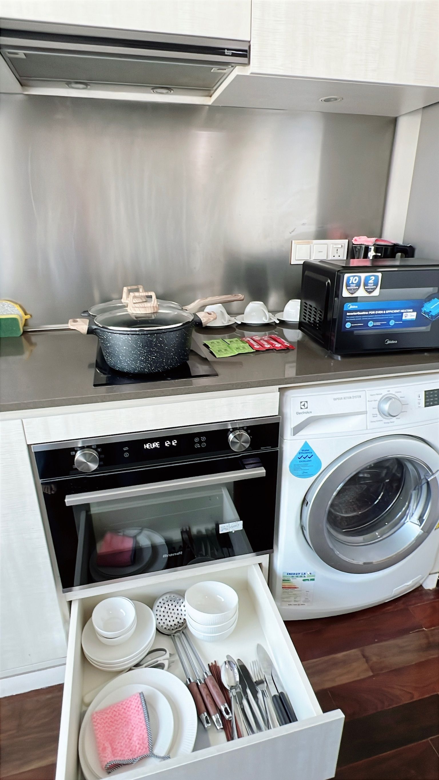 Kitchen with open drawer holding dishes, pot on stovetop, oven, washing machine, and microwave.