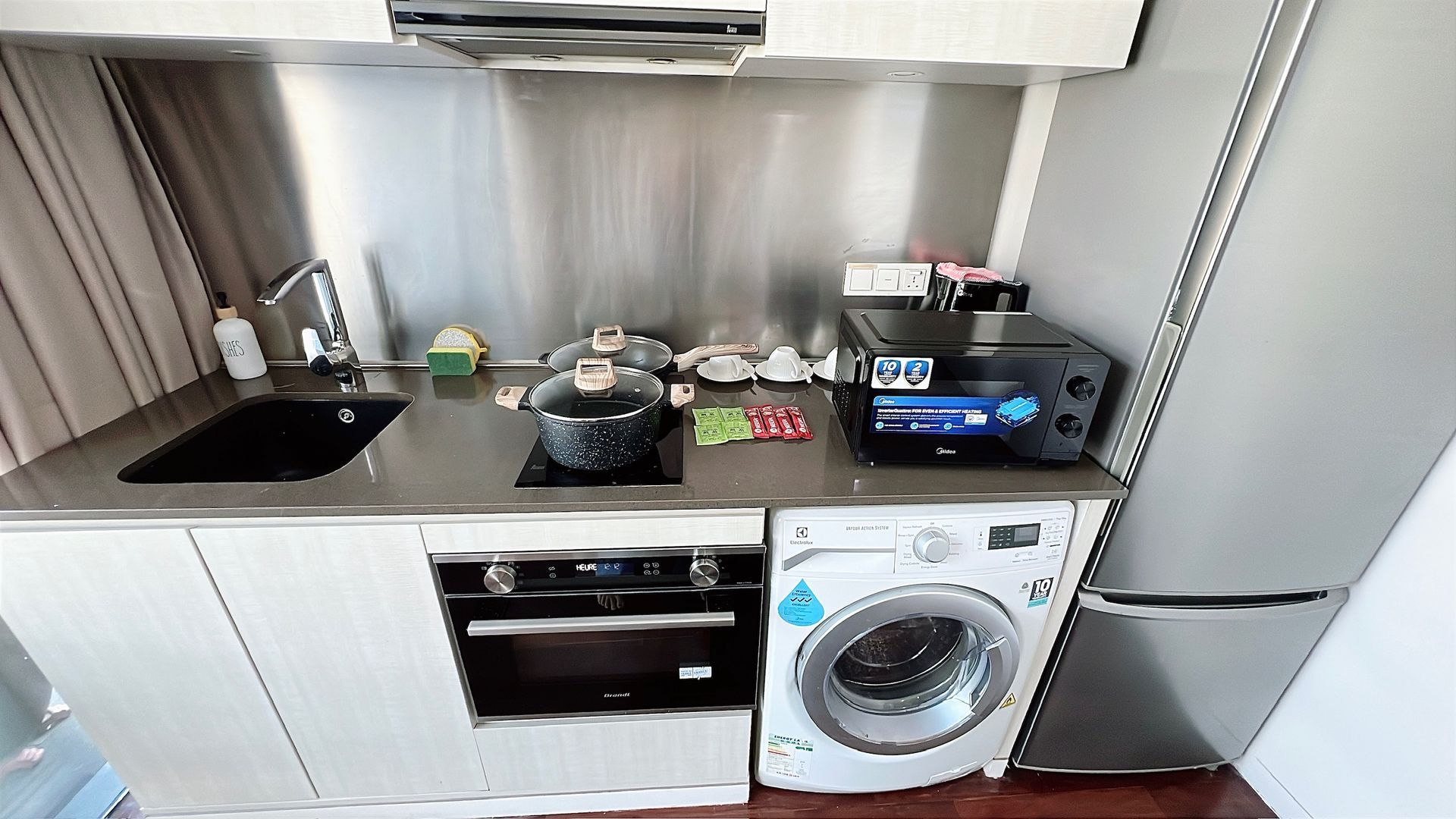 Small kitchen with a stove, oven, microwave, and washing machine. Stainless steel backsplash.