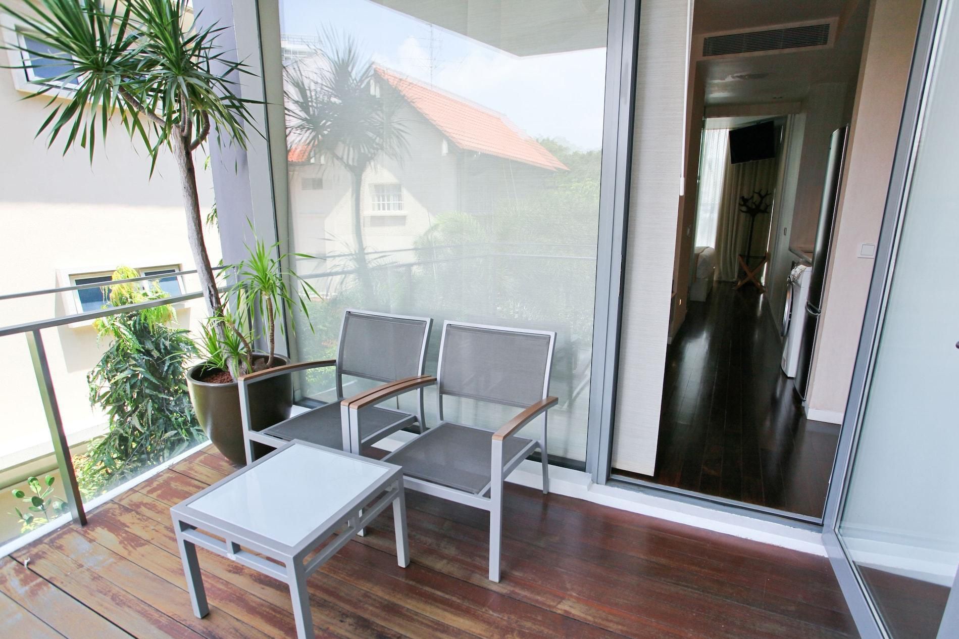 Balcony with two chairs, a small table, plants, and a view of a house through a glass door.