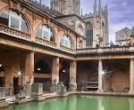 The Roman Baths, Bath, England: stone ruins surround a pool of green water, with Bath Abbey in the background.