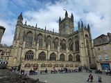 Bath Abbey exterior, gothic architecture with tall windows, people seated in the square under a cloudy sky.