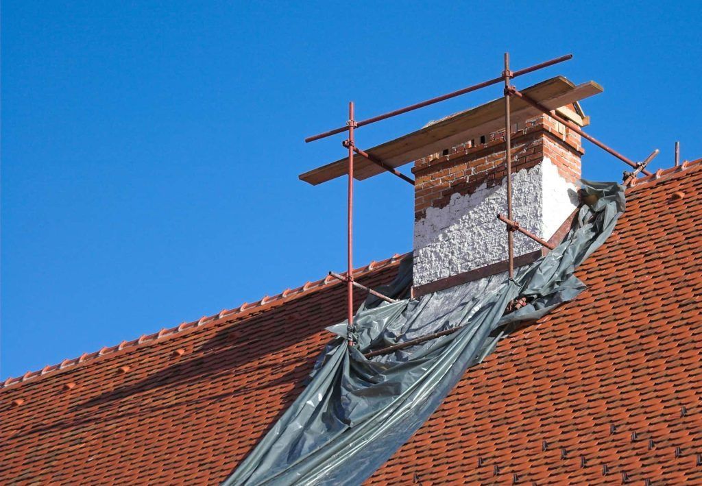 Chimney on a red tiled roof being repaired, covered by a tarp, with scaffolding.