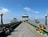 Wooden pier extending into water with ornate structures, under a blue sky.