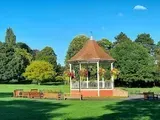 Bandstand in a park on a sunny day. Green grass, trees, and blue sky.