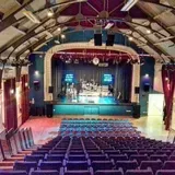 Inside a theater: Stage with band, audience seating, arched ceiling.