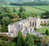Stone abbey building surrounded by green trees and fields.