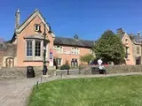 Pink building with a bay window, set on a lawn with a person sitting on a bench. Blue sky.