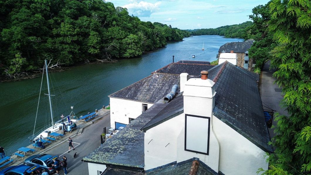 Buildings on a waterfront, cars parked along the road, water and trees in the background.
