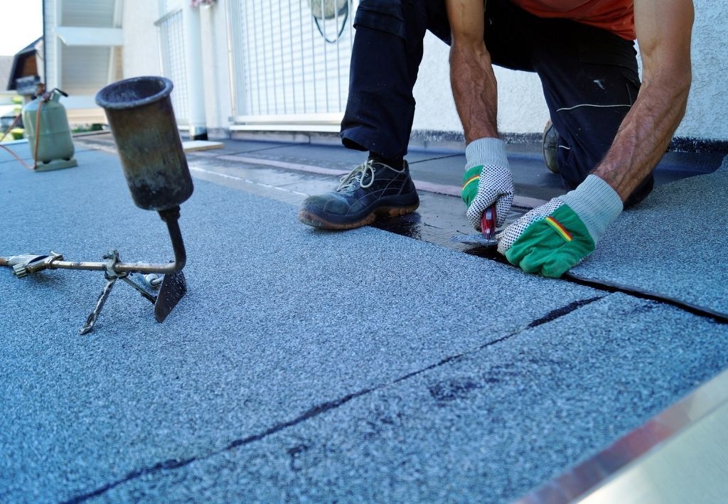 Person on rooftop applying sealant to roofing seams with a torch.