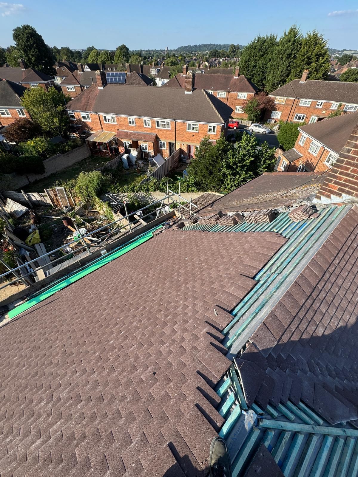 Rooftop view over terraced houses, with blue-gray roof panels in the foreground and trees beyond.