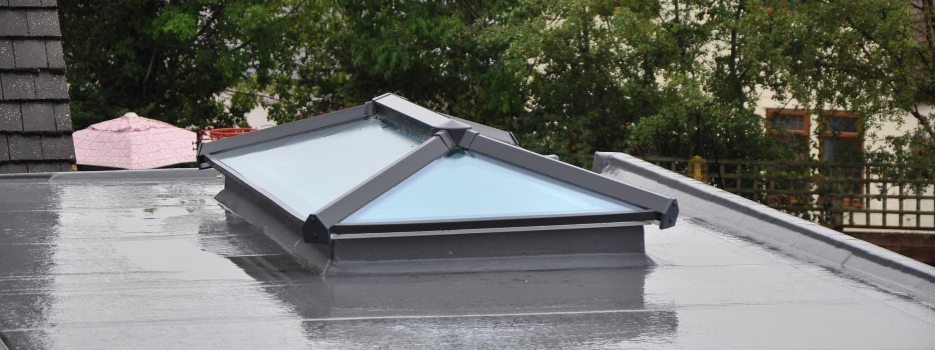 Skylight on a flat roof, with a pink object on the roof near a chimney. Trees are visible in the background.