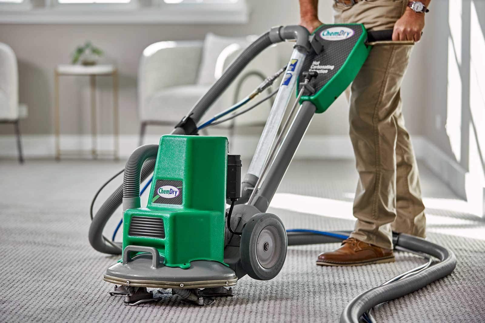 A Chem-Dry technician is using a green and gray carpet cleaning machine on a carpeted floor.