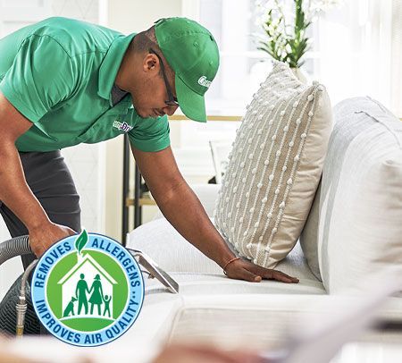 A Chem-Dry technician cleans a white couch with a vacuum, promoting allergy removal and improved air quality in a home.