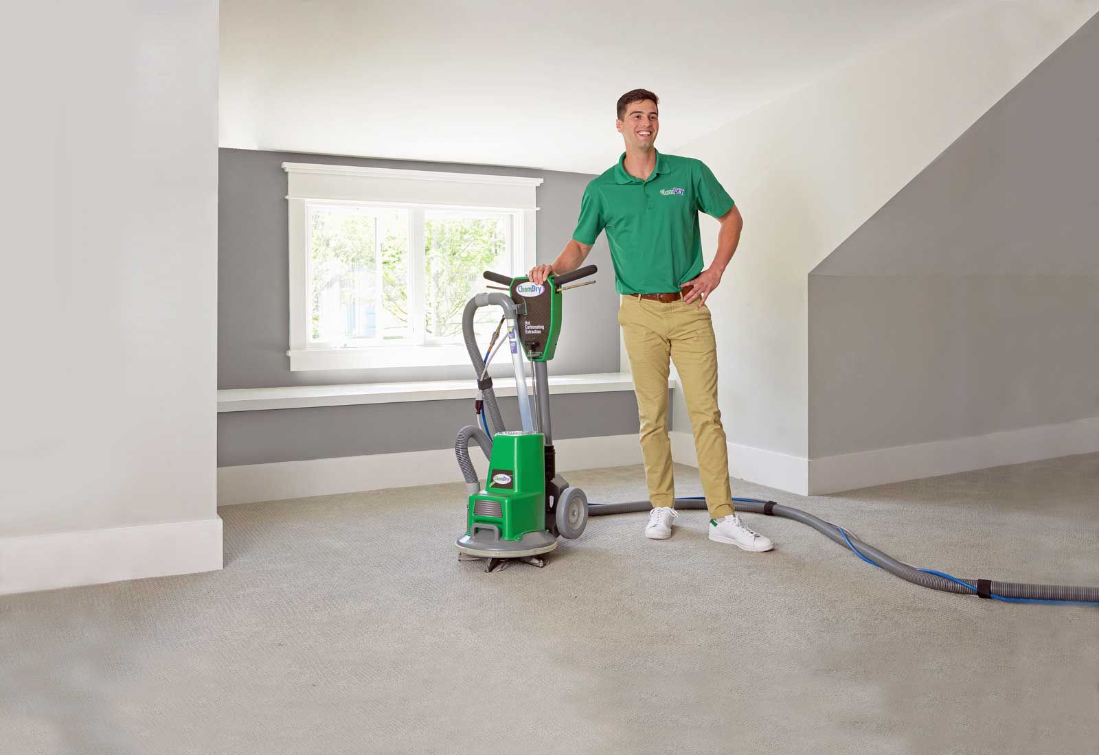 A Chem-Dry technician operating a green carpet cleaning machine in a room with light gray walls and carpet.