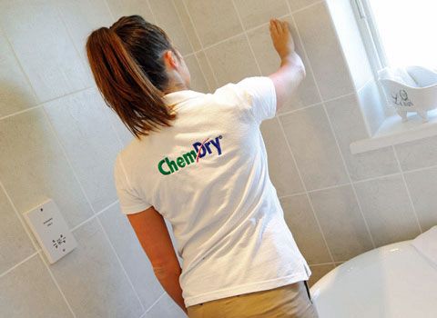 A Chem-Dry technician is cleaning bathroom tile by a window.