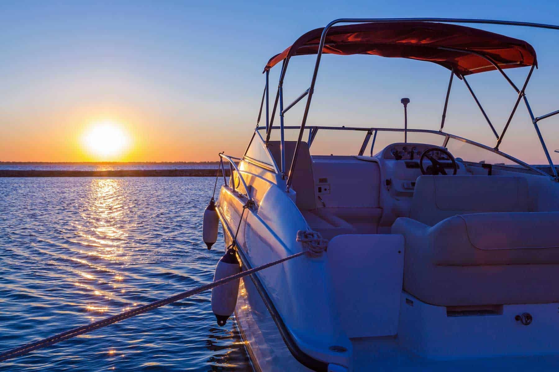 A motorboat docked on a calm ocean at sunset, with the sun reflecting on the water.